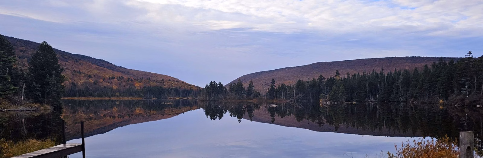 Calm pond reflecting forested hills at dusk in the White Mountain National Forest