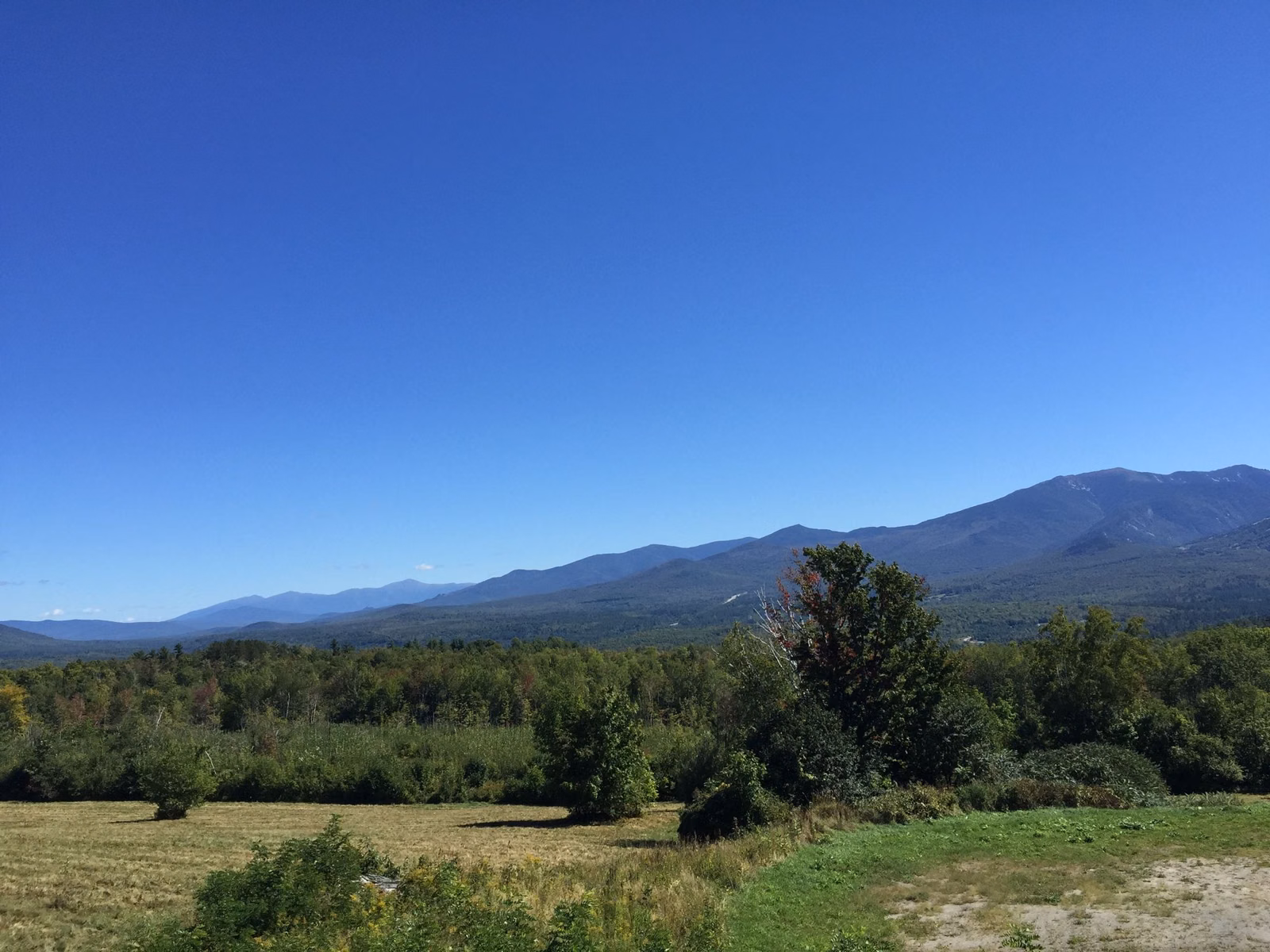 Franconia Ridge on the horizon beyond green fields and trees under a clear sky